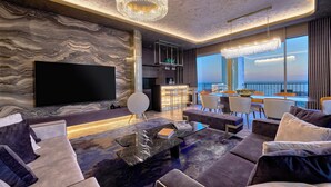 A modern living room with a large flat-screen TV, marble wall, and a view of the city. - Merit Starlit Hotel Casino & SPA (Budva)