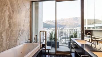 A modern bathroom with a large bathtub, two sinks, and a view of a cityscape through large windows.