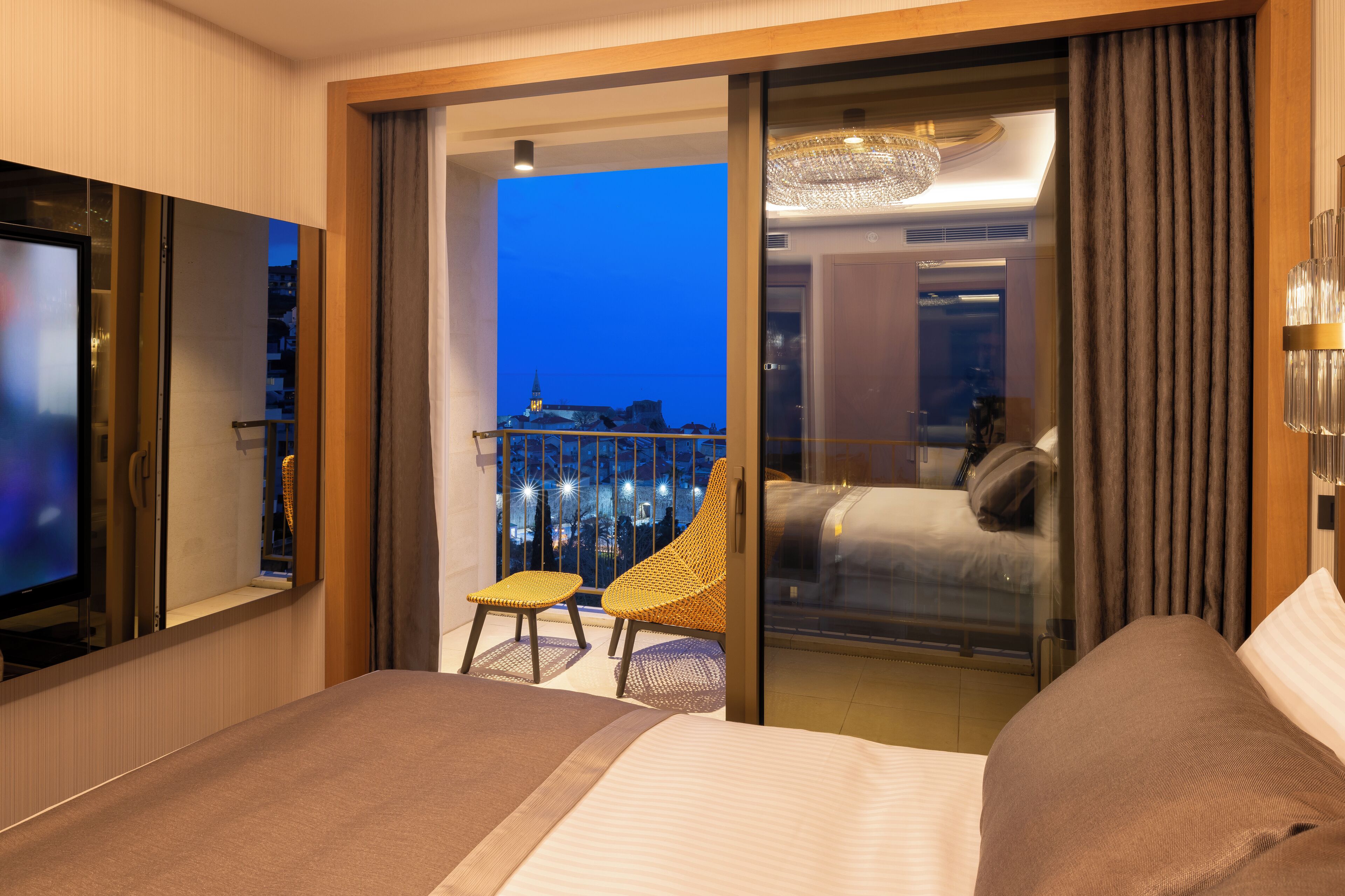 Una camera d'albergo con un letto, una TV, un balcone e vista sulla città, e una sedia.