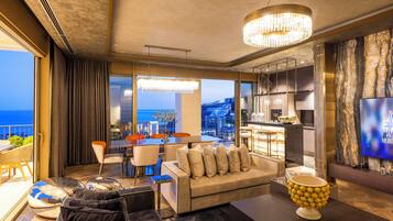 Una sala de estar moderna con sofá, comedor con mesa y sillas, zona de cocina y un televisor grande en la pared.
