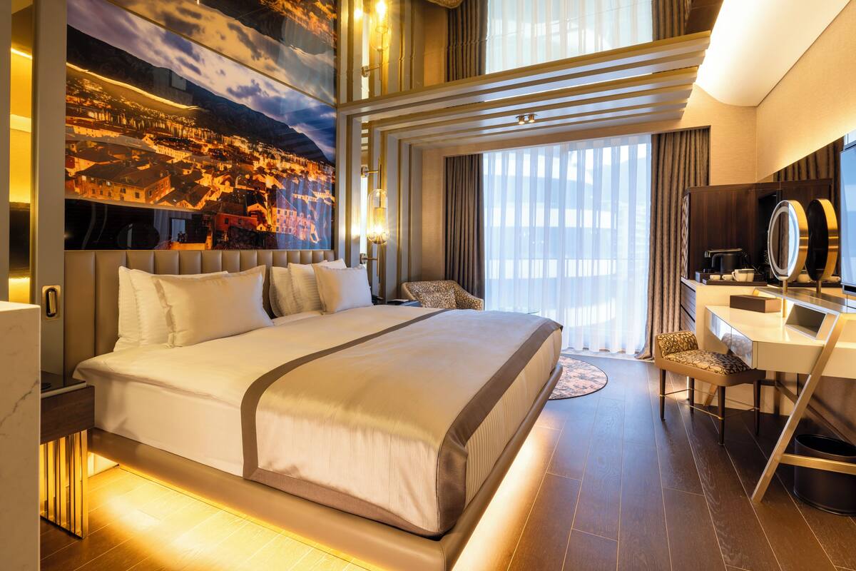 Une chambre d’hôtel moderne avec un grand lit, un bureau doté d’un miroir et une fresque représentant un paysage urbain sur le mur.