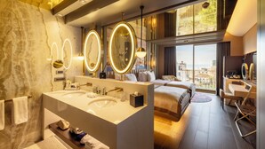 A modern hotel room with a large bed, a vanity with multiple mirrors, a large window with a city view, and a desk with a chair. - Merit Starlit Hotel Casino & SPA (Budva)