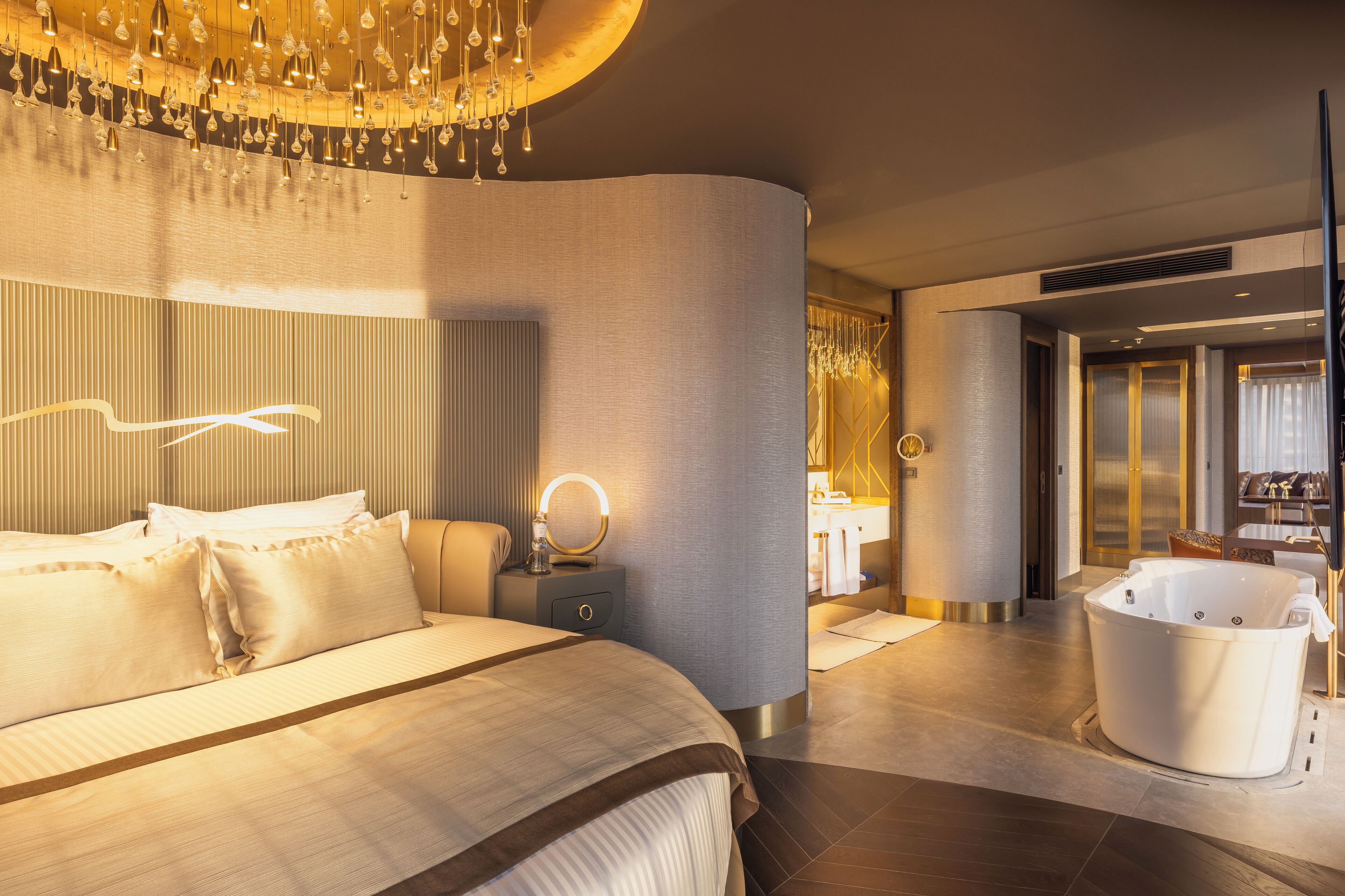 Moderni hotellihuone, jossa on suuri sänky, peilillä varustettu meikkipöytä, kylpyamme ja kattokruunu.