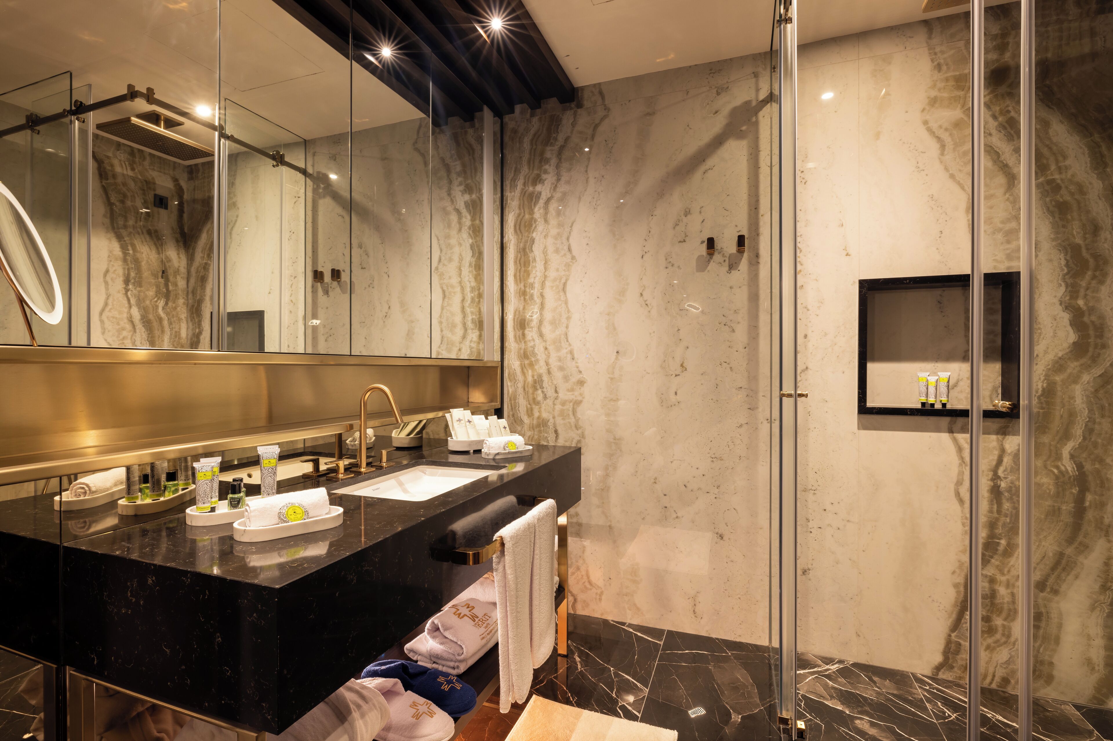 A modern bathroom with a black marble countertop, two sinks, a large mirror, and a glass shower enclosure.