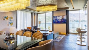 A modern hotel room with a large window offering a mountain view, a dining area with a glass table, and a seating area with a TV. - Merit Starlit Hotel Casino & SPA (Budva)