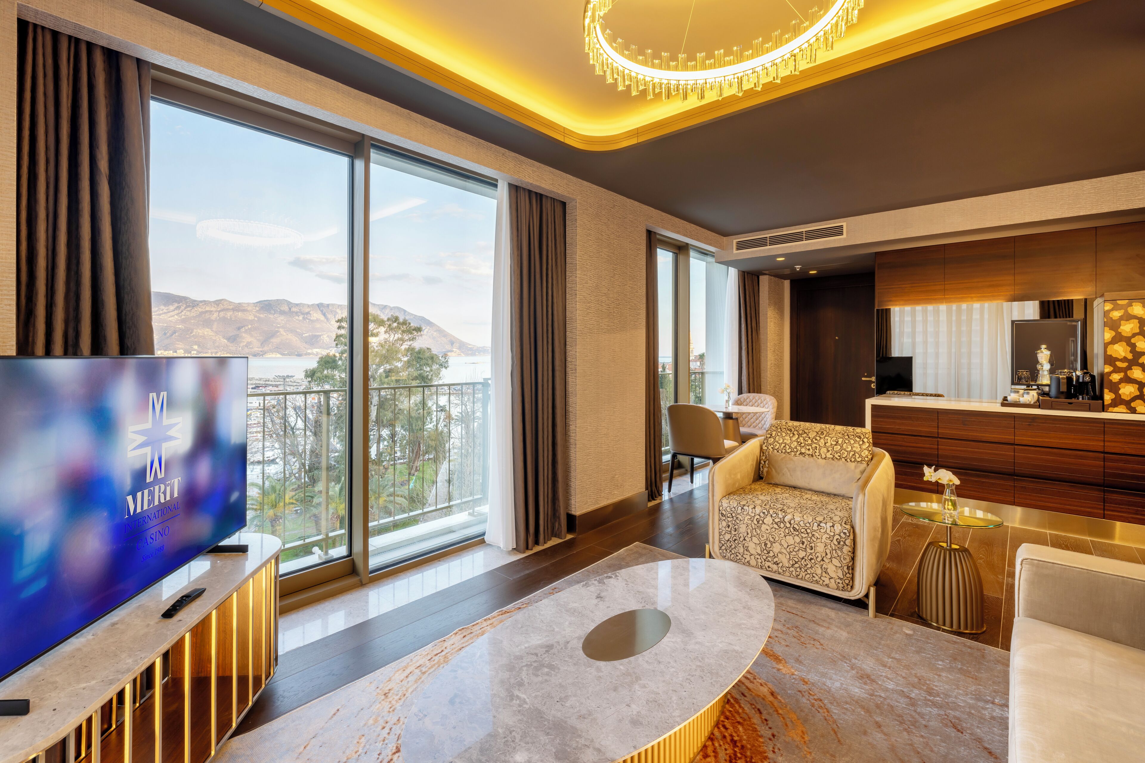 Habitación de hotel moderna con un televisor grande, asientos cómodos, una zona de comedor y vistas al exterior.