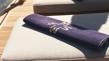 A row of sun loungers with towels, wooden deck, and umbrellas, overlooking a body of water with mountains in the background.