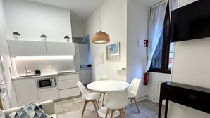 A modern kitchen with white cabinets, a dining table with four chairs, a hanging light fixture, and a flat-screen TV mounted on the wall. - Corazón Donostiarra (Donostia)