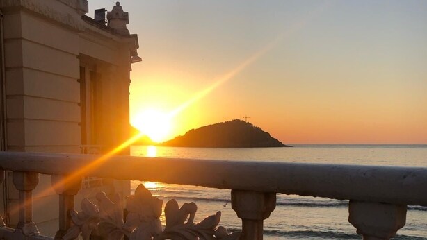 A sunset view from a balcony with ornate metal railings, overlooking a beach and a distant island. - Corazón Donostiarra (Donostia)