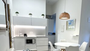 A modern living room with a white sofa, a dining table with white chairs, and a kitchen area with white cabinets and appliances. - Corazón Donostiarra (Donostia)