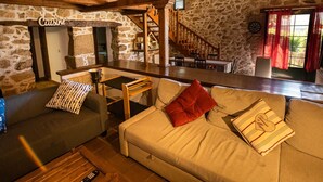 Un espacio de sala acogedor con pared de piedra, una escalera de madera y una zona de bar.