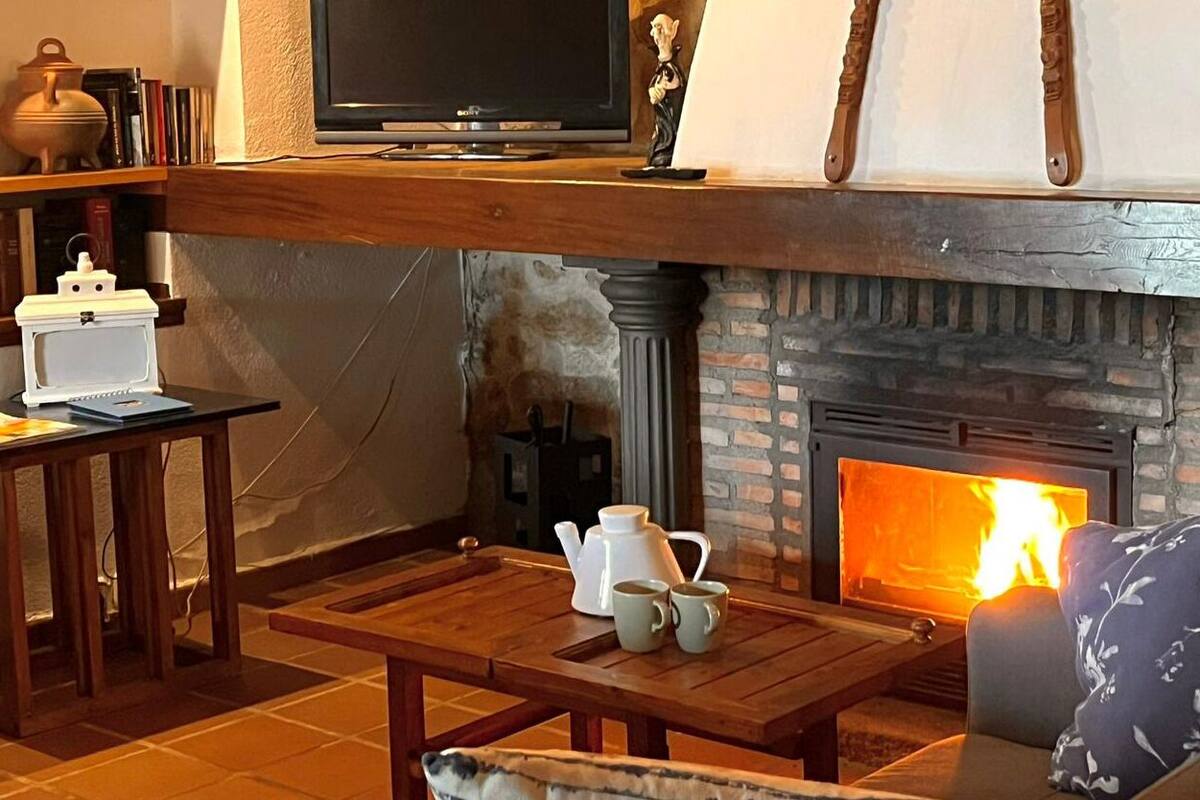 A cozy living room with a fireplace, a television, and a coffee table with teapots.