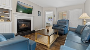 Een woonkamer met een open haard, blauwe banken, een flatscreen-televisie en een houten salontafel.