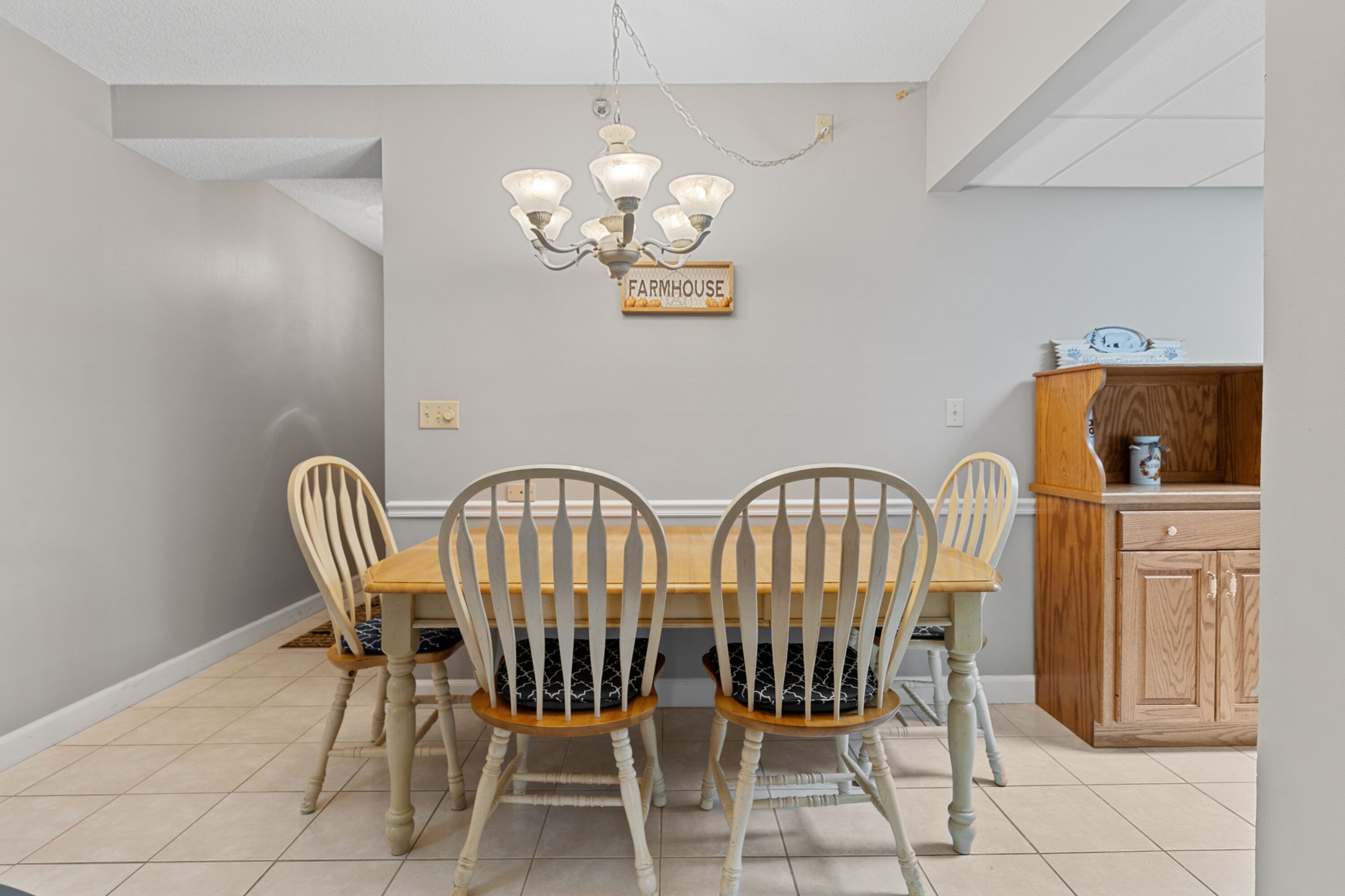 Een eetruimte met een houten tafel en vier stoelen, een kroonluchter en een keuken met houten kastjes.