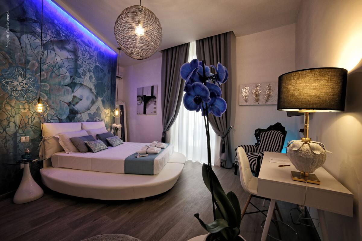 Une chambre moderne avec un lit aux lignes courbes, un bureau et une grande fenêtre agrémentée de rideaux.