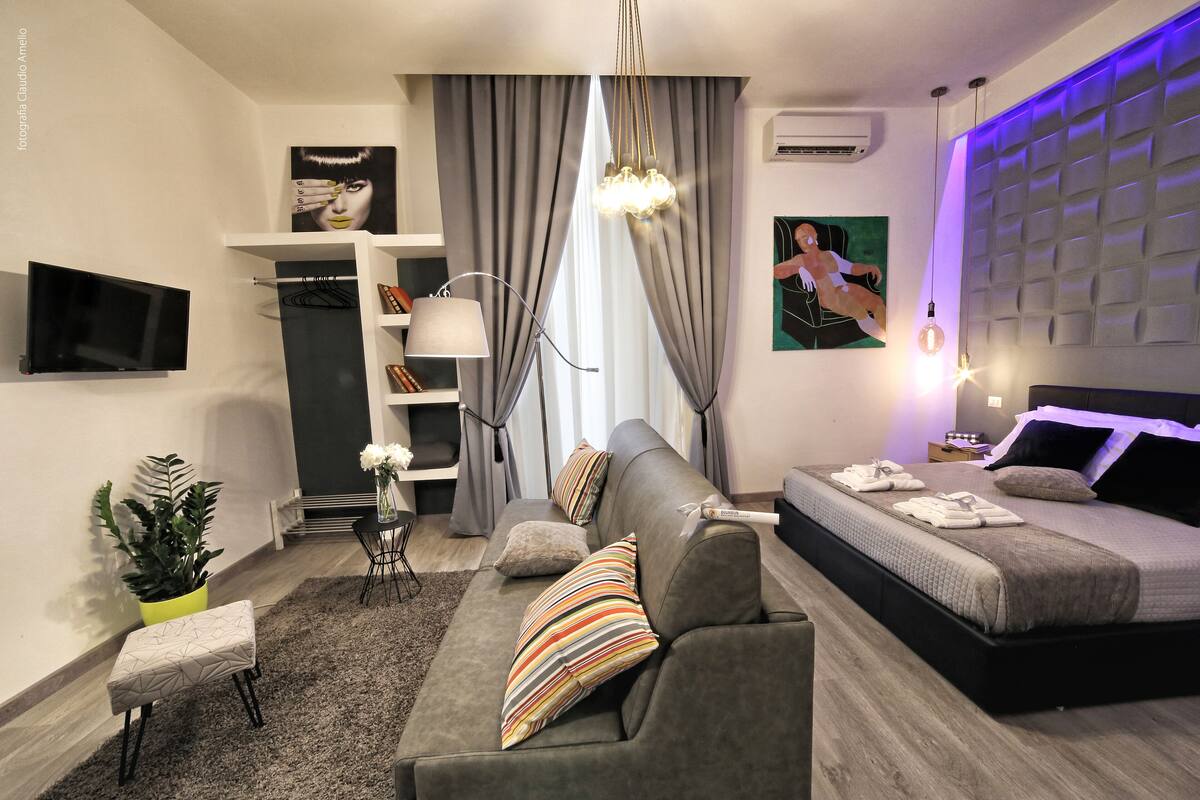Une chambre moderne avec un canapé, un lit, une télévision, une plante et une fenêtre avec des rideaux.