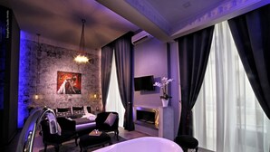 A modern bathroom with a freestanding bathtub, a seating area with a sofa and armchairs, a fireplace, and a large window with curtains. - Bourbon House (Naples)