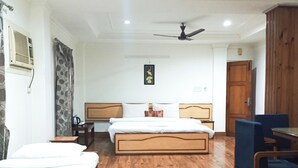 Una camera d'albergo con pavimento in legno, un letto con testiera in legno, una scrivania con sedia, un armadio e una ventola a soffitto.