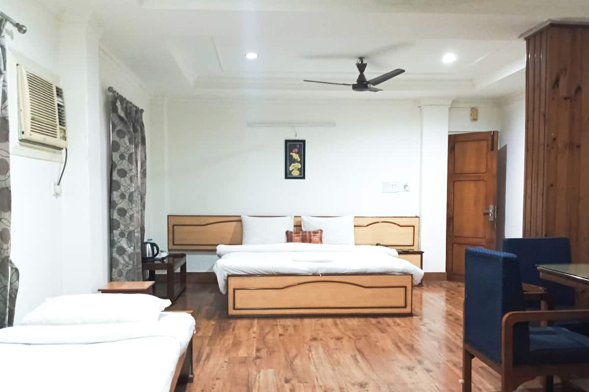 A hotel room with a wooden floor, a bed with a wooden headboard, a desk with a chair, a wardrobe, and a ceiling fan.