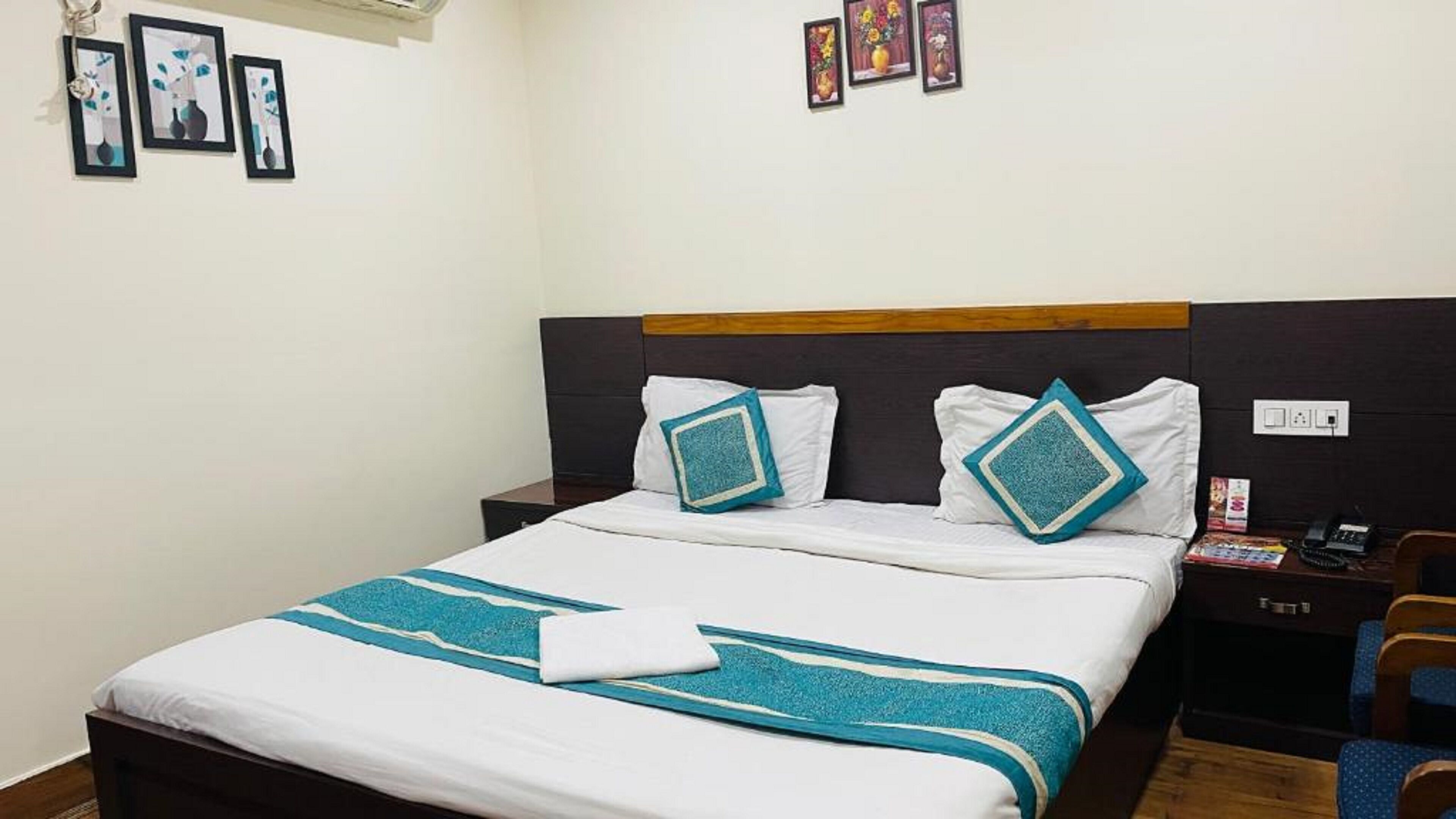 Una habitación de hotel con cama, mesita de noche, una silla y una obra de arte en la pared.