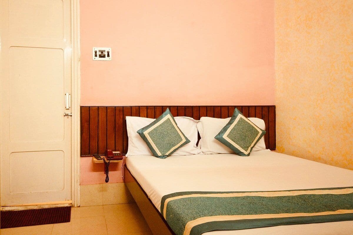 A single bed with a wooden headboard, two pillows, a bedside telephone, and a green and beige bedspread.