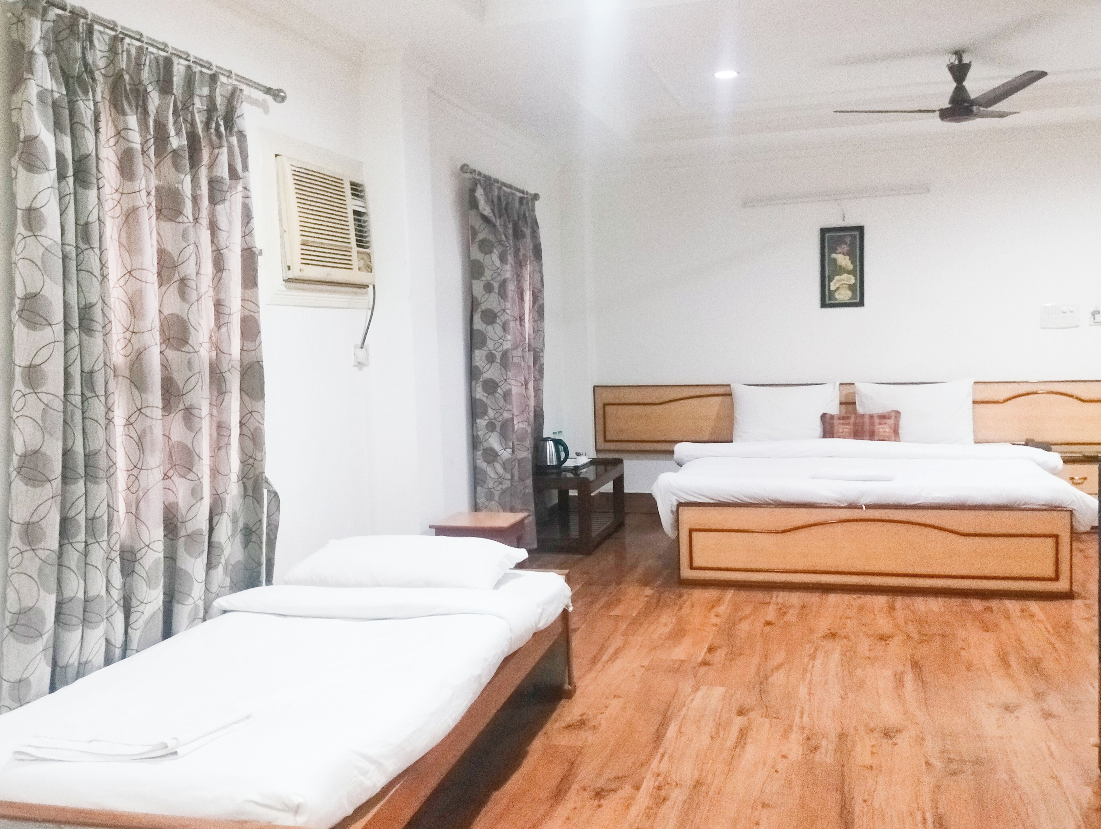 A hotel room with two single beds, a ceiling fan, a small table, and a nightstand.