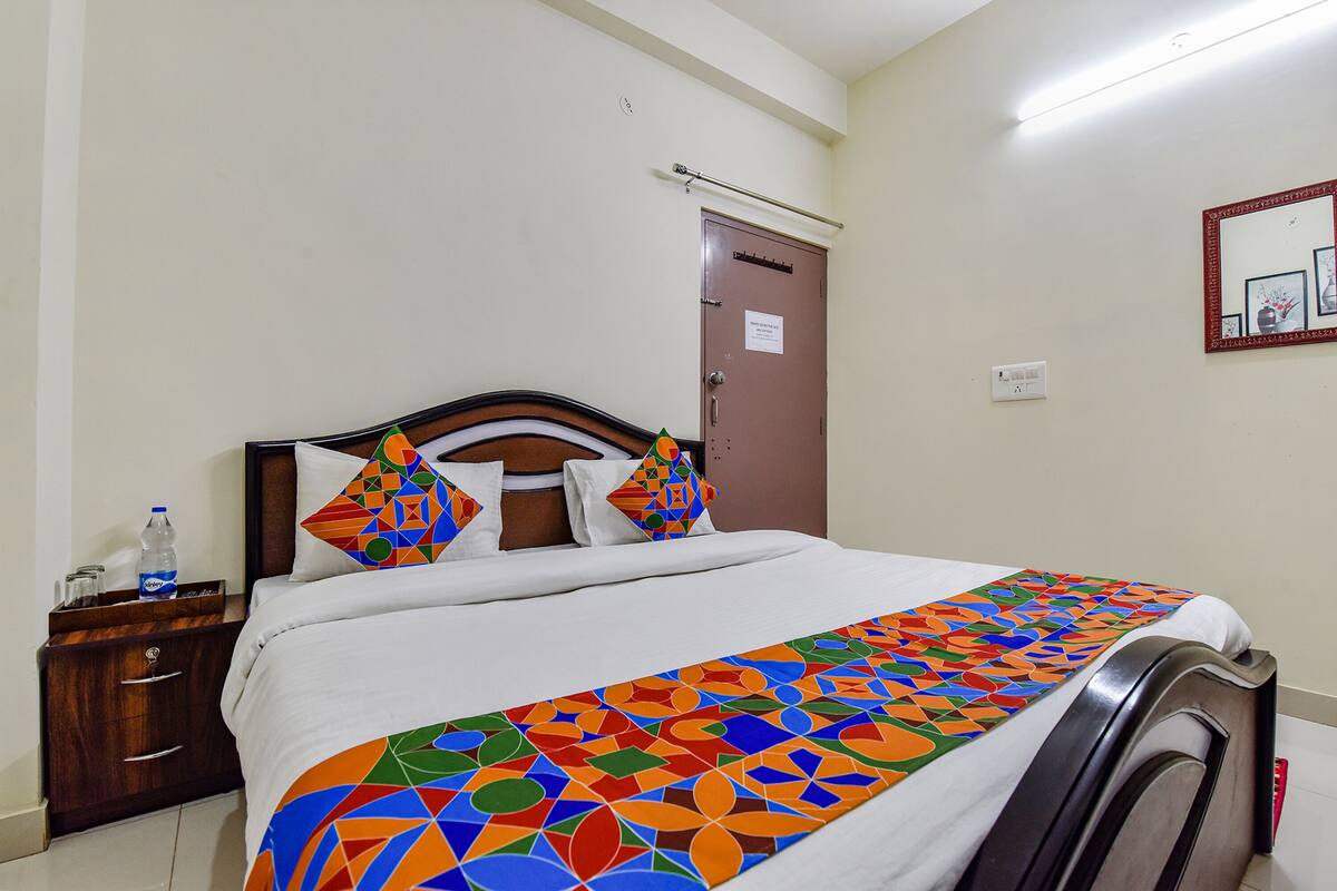 A hotel room with a bed, a wooden nightstand, a water bottle, and a door.