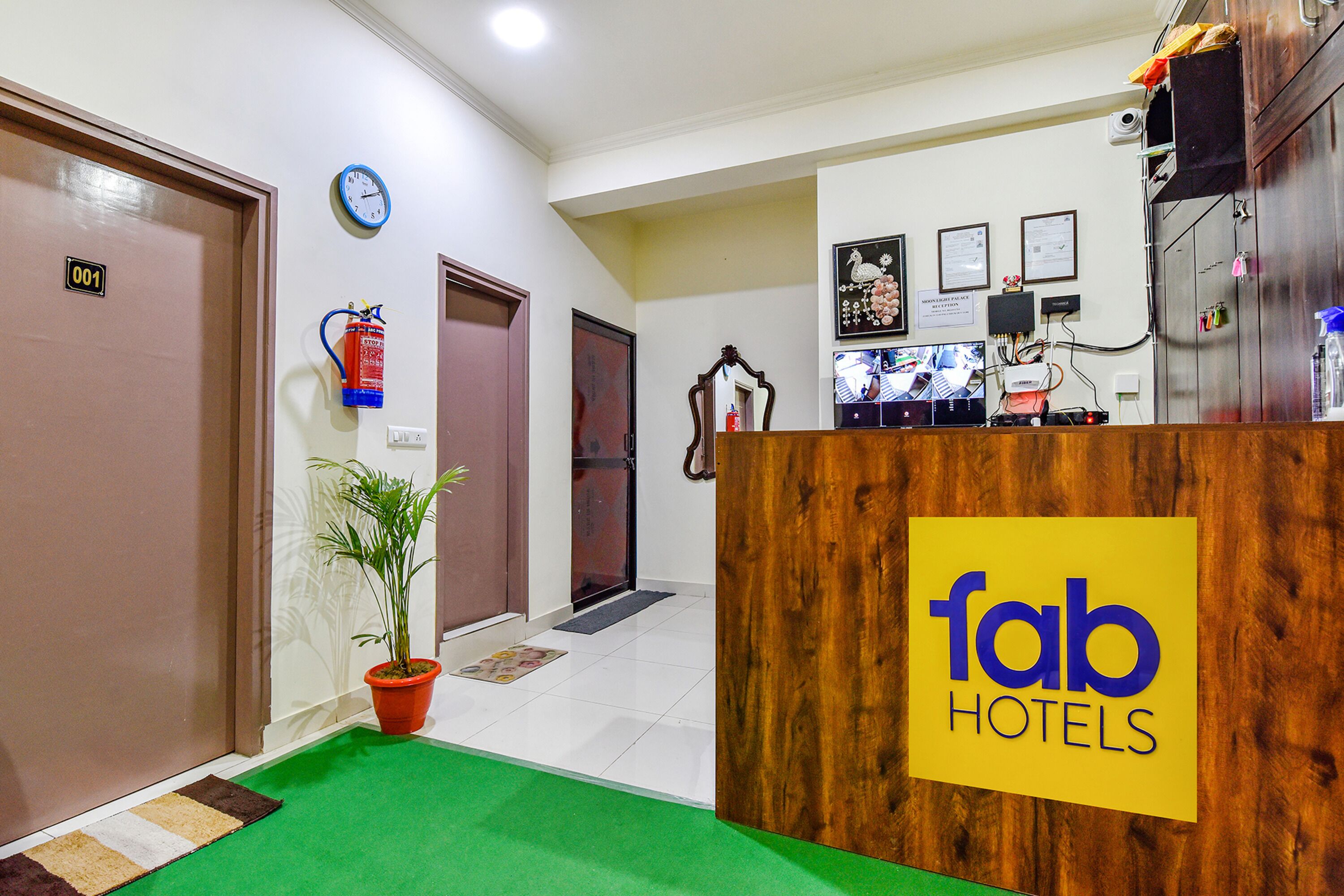 A hotel reception area with a wooden reception desk, a potted plant, and a clock on the wall.