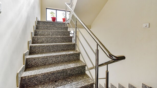 A staircase with granite steps and a metal handrail, leading to a landing with a window and potted plants. - Fabhotel Moon Light Palace (Jaipur)