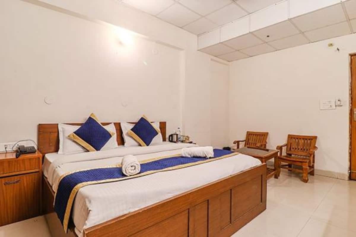 Una habitación de hotel con una cama grande, dos sillas de madera, una mesita de noche de madera y un armario de madera.