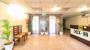 Uma área de recepção de hotel com balcão de check-in, um banco de madeira e plantas em vasos.