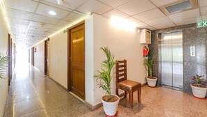 Corredor de hotel com porta de madeira, um banco e plantas em vasos.