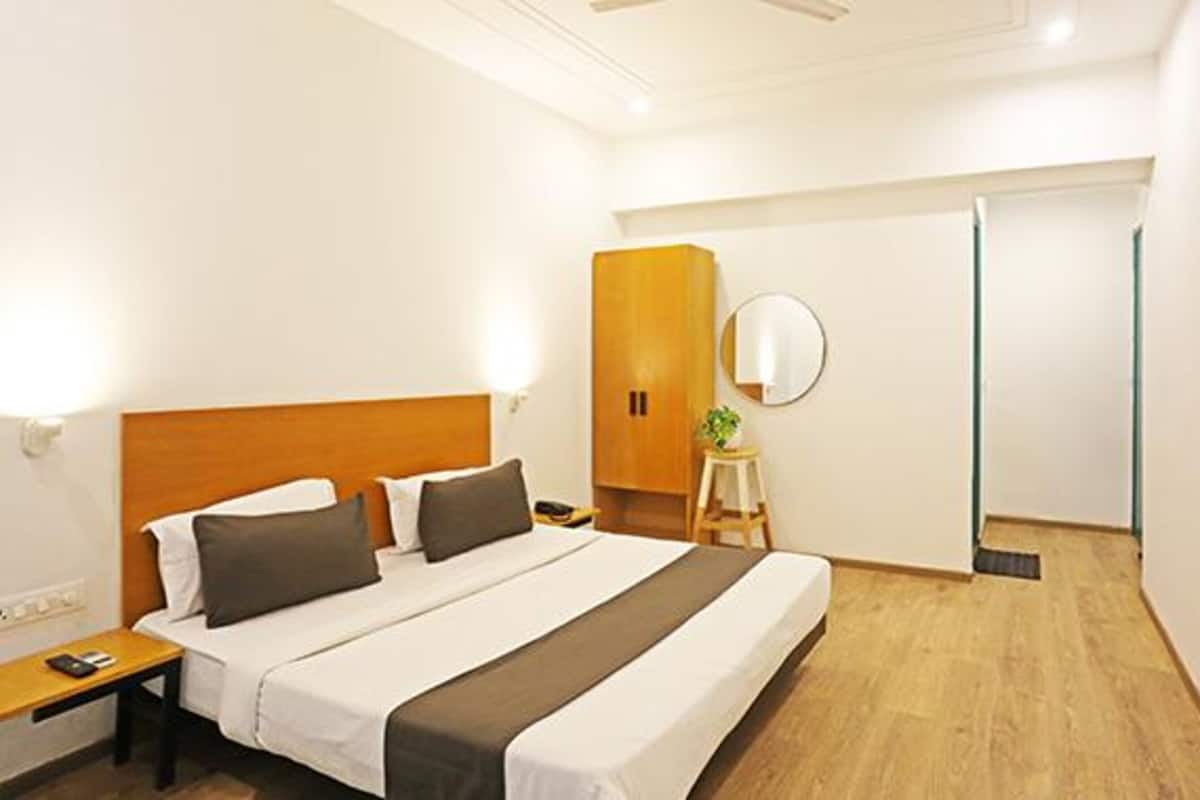 A hotel room with a bed, bedside table, nightstand, wardrobe, and a mirror.