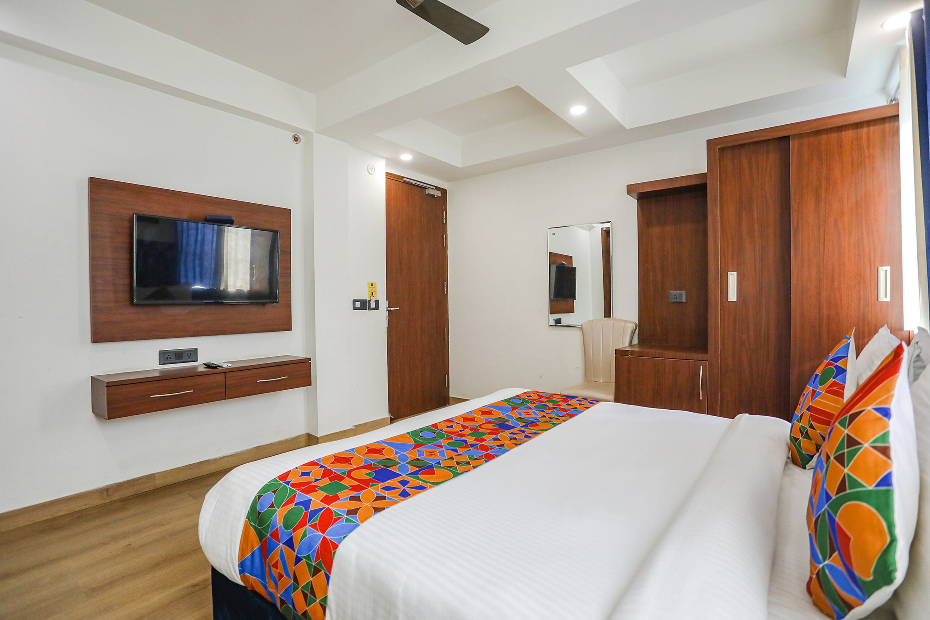 A hotel room with a bed, a TV mounted on the wall, a wardrobe, and a mirror.