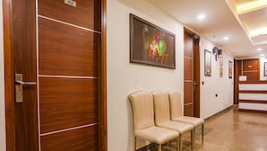A hotel hallway with wooden doors, a framed abstract painting, and a seating area with chairs. - FabHotel RS Golden (New Delhi)
