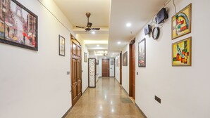 A hallway with polished floors, ceiling fans, and framed artwork on the walls. - FabHotel RS Golden (New Delhi)
