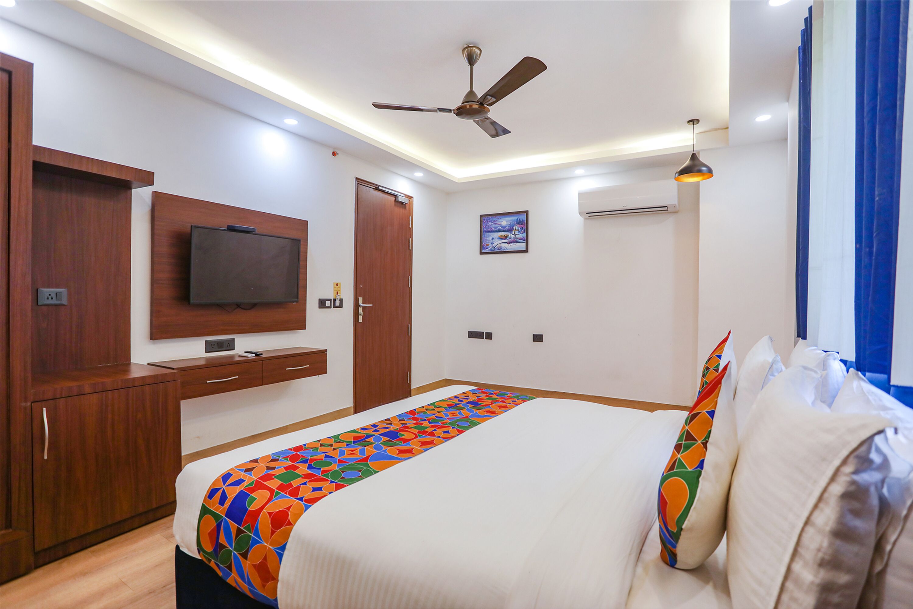 A hotel room with a bed, a ceiling fan, a mounted TV, and a window with curtains.