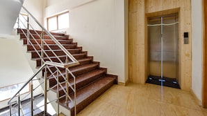 A staircase with metal railings leading to an elevator in a building with wooden paneling and a tiled floor. - Fabhotel Manali Heaven (Manali)