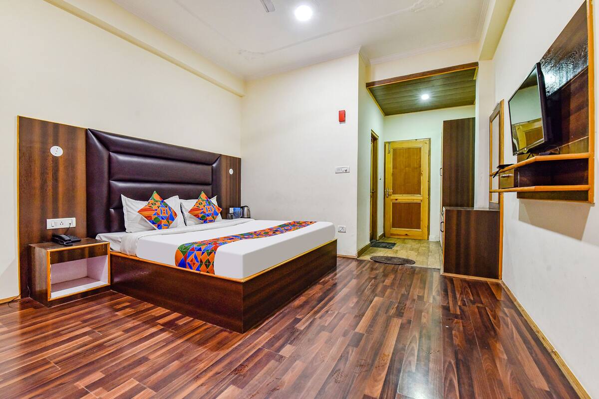 A bedroom with a wooden bed, a nightstand, a TV mounted on the wall, and a wooden door leading to another room.