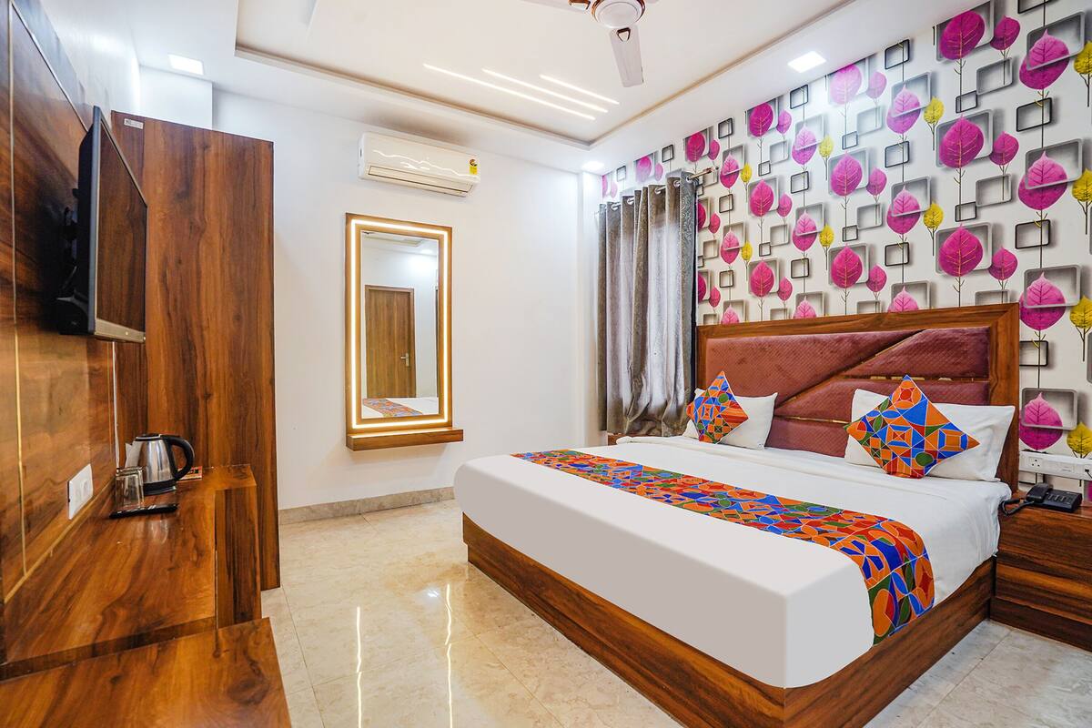 A hotel room with a wooden wardrobe, a bed with a colorful bedspread, a large mirror, and a wall with a leaf pattern.
