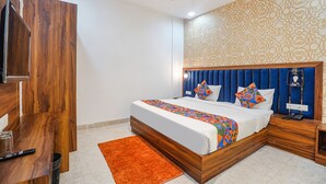 A bedroom with a wooden bed frame, a patterned wall, and a ceiling fan. - Fabhotel Grand Inn Ii (Agra)