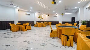 A spacious hall with multiple round tables and yellow chairs, air conditioning units, and ceiling fans. - Fabhotel Grand Inn Ii (Agra)