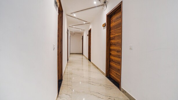 A hallway with white walls, wooden doors, and a marble floor. - Fabhotel Grand Inn Ii (Agra)