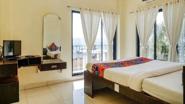 A hotel room with a bed, a desk, a chair, a TV, and a large window with curtains. - FabHotel Chinar Residency (Jaoli)