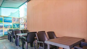 An outdoor seating area with tables and chairs, a tiled floor, and a wall with a poster. - FabHotel Chinar Residency (Jaoli)