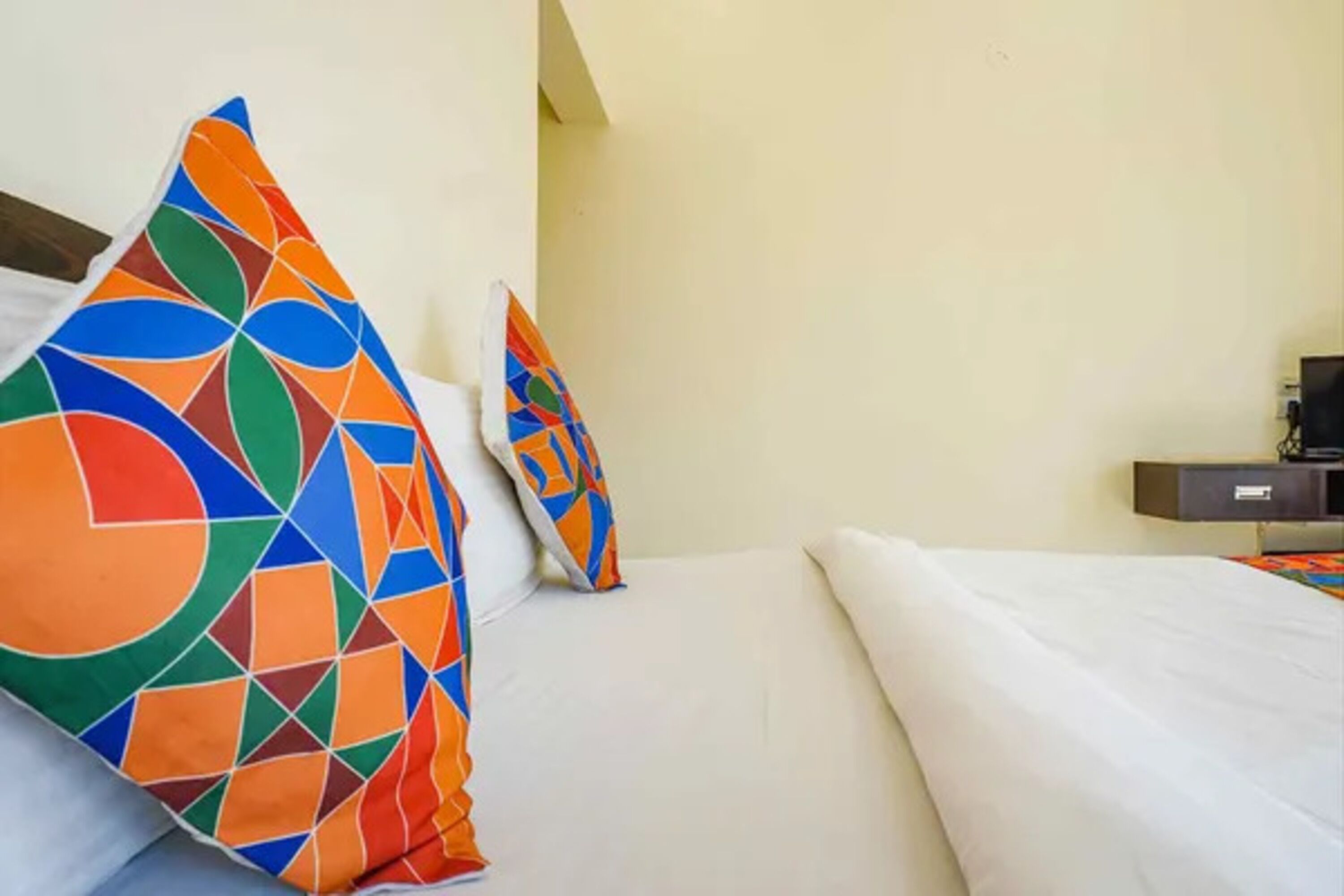A hotel room with a bed, pillows, a TV, and a desk.
