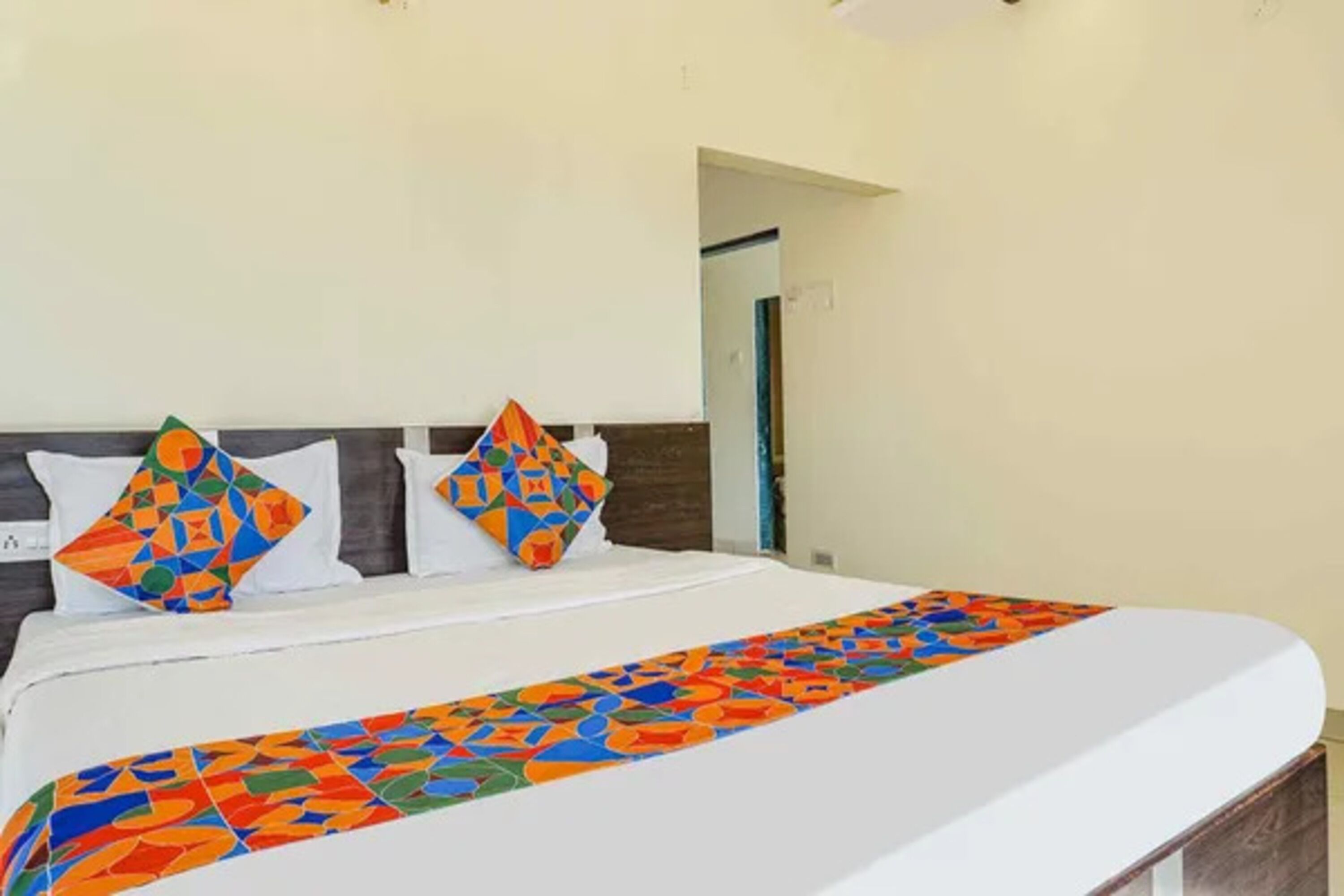 Ein Bett mit farbenfroher geometrischer Stegdecke und Kissen, ein weißer Kopfteil und ein Spiegel an der Wand.