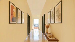 A hallway with framed artwork on the walls, a polished floor, and a table with books and decorative items. - FabHotel Chinar Residency (Jaoli)