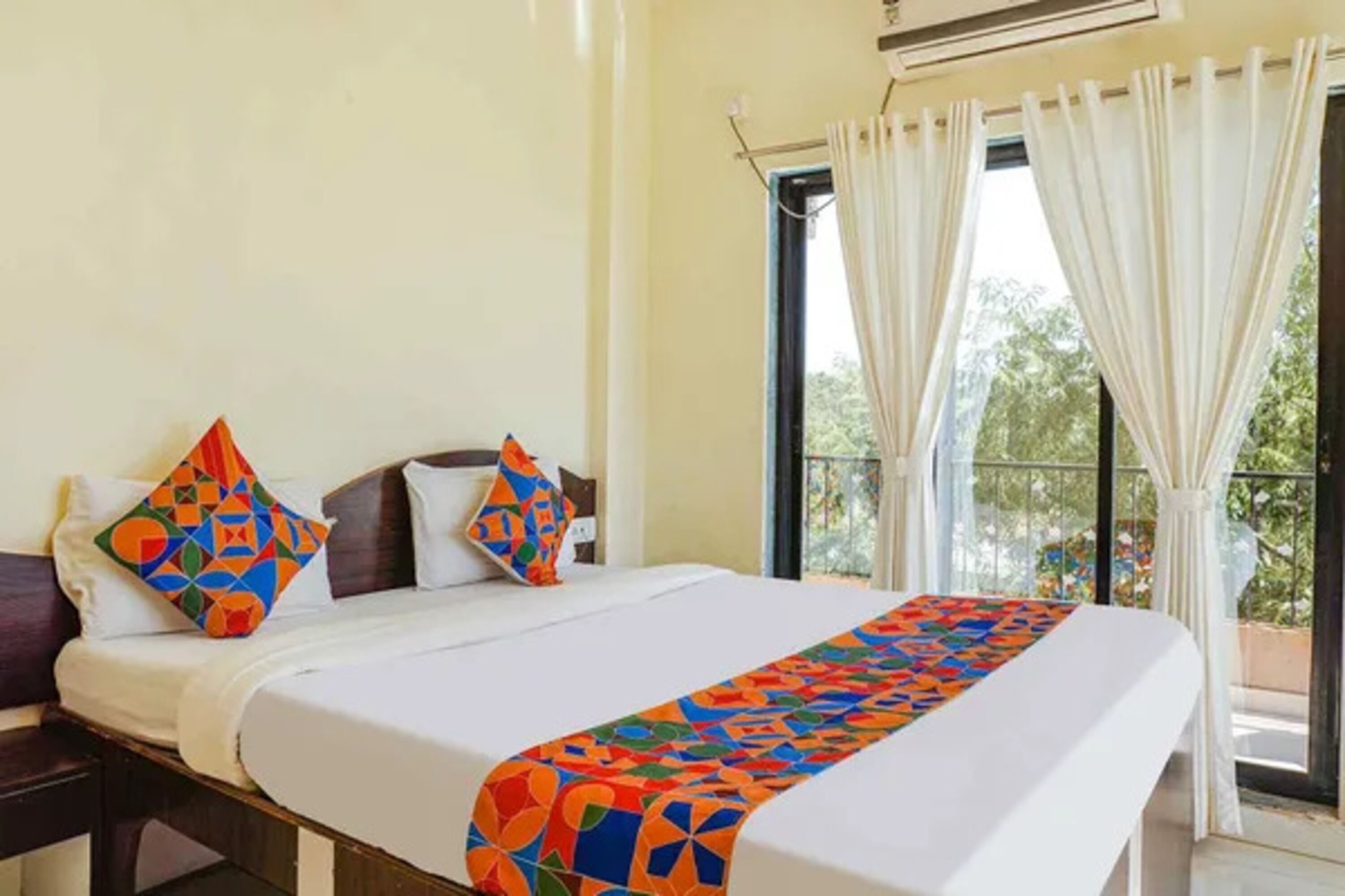 A hotel room with a bed, pillows, a window with curtains, and a view of greenery outside.