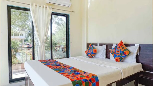 A hotel room with a bed, a window with curtains, and an air conditioning unit.
